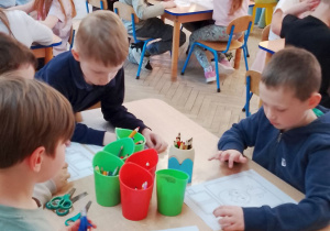 Dzieci z grupy IV siedzą przy stolikach i wykonują pracę plastyczną o książce.