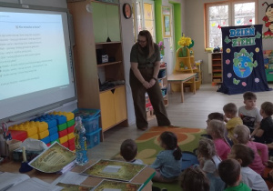 Dzieci słuchają ciekawych informacji na temat lasu siedząc na dywanie.