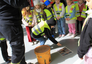 Julek przykucnął obok gazety i sypie sorbent na rozlany olej. Grupka dzieci obserwuje działanie kolegi.