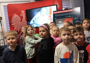 Dzieci stoją na tle tablicy interaktywnej.