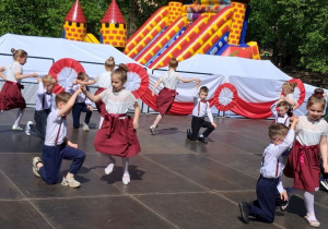 Chłopcy klękają na kolano, a dziewczynki tańczą wokół nich.