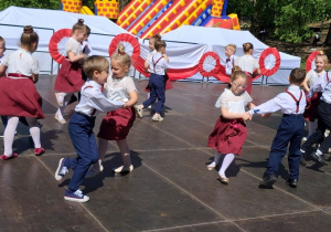 Dzieci tańczą na scenie w kółeczkach.