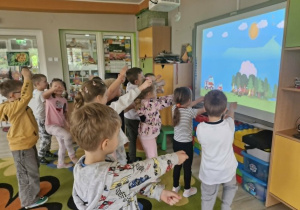 Dzieci stoją przed tablicą multimedialną w trakcie zabawy ruchowej do piosenki "Strażak".