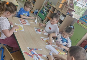 Dzieci siedzą przy stoliku w trakcie kolorowania obrazka przedstawiającego wóz strażacki.