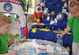 Nikola i Oliwier wlewają do słoików z watą farbę. W tle dekoracja z okazji Dnia Kosmosu.