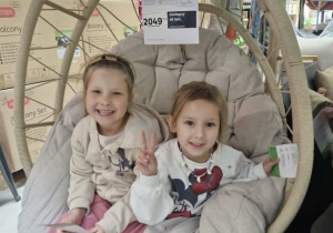 Maja i Zuzia pozują do zdjęcia siedząc w wiszącym fotelu ogrodowym.