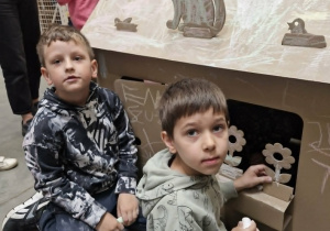 Franek i Wojtuś malują kredami duży domek wykonany z tektury.