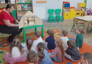 3. Dzieci siedzą na dywanie i słuchają opowieści o Misiu Wojtku przedstawianej z wykorzystaniem Teatrzyku Kamishibai.