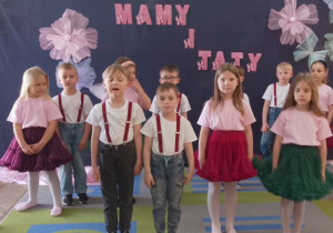 Czworo dzieci stoi na środku sceny i recytuje wiersz. Za nimi stoją rówieśnicy.