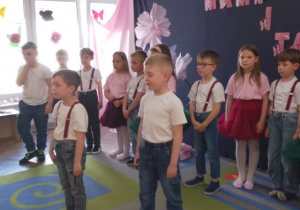 Dwóch chłopców stoi na środku sceny i recytuje wiersz. Za nimi stoją rówieśnicy na tle dekoracji.