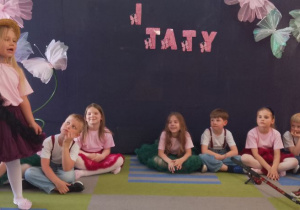 Tosia i Mikołaj występują na scenie w roli Czapli i Żurawia. Obok chłopca leży wędka. Pozostałe dzieci siedzą na dywanie.