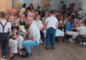 Rodzice siedzą przy udekorowanych stołach, a dzieci wręczają im upominki.