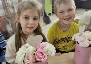 Oliwia i Wojtuś siedzą przy stoliku. Przed dziećmi stoją bukiety z kwiatów mydlanych.