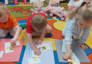 Olek, Szymon i Marysia na dywanie układają puzlle z wizerunkiem pszczoły.