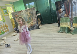 Liliana stoi na środku sceny. W tle widać dekoracje do spektaklu.