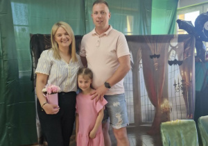 Oliwia pozuje do zdjęcia ze swoimi rodzicami na tle dekoracji zamku.