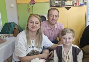 Oluś siedzi przy stoliku razem ze swoimi rodzicami.
