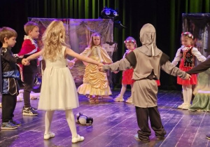 Dzieci stoją na scenie w kółku trzymając się za ręce.