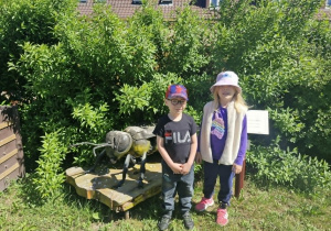 Antoś i Nadia w ogrodzie przedszkolnym stoją obok rzeźby pszczoły.