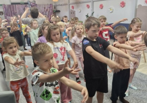 3.Dzieci z rękami wyciągniętymi przed siebie uczestniczą w rozgrzewce.