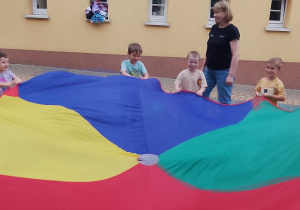 Dzieci z panią Karoliną bawią się w zabawy z chustą animacyjną.