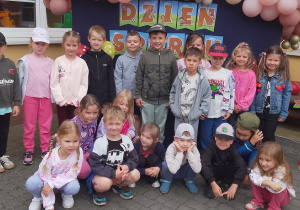 Biedronki pozują do zdjęcia grupowego. W tle baner z napisem dzień sportu i balony.