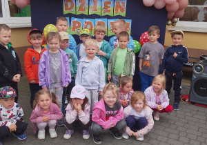 Motylki pozują do grupowego zdjęcia. W tle baner z napisem dzień sportu oraz balony.