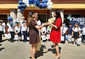 Dwie mamy dziękują mamie Mikołaja za pracę na rzecz grupy i wręczają bukiet kwiatów. W tle stoją dzieci oraz Pani dyrektor.