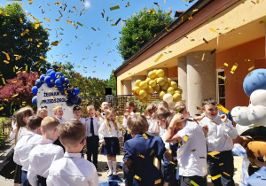 Dzieci stoją na tarasie, a nad nimi wiruje confetti.