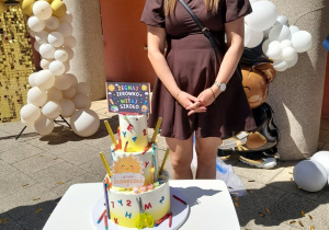 Mama Nadii stoi na tarasie, a przed nią tort z napisem "Żegnaj zerówko, witaj szkoło".