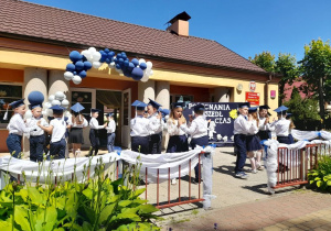 Dzieci na tarasie przedszkolnym tańczą w parach przy piosence. W tle budynek przedszkola i fragment dekoracji.