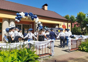 Dzieci tańczą w kole Poloneza. W tle budynek przedszkola, dekoracja.
