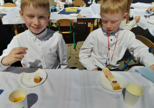 Dwóch chłopców siedzi przy stole i degustuje tort.