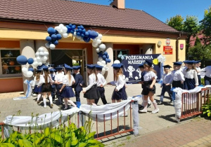 Dzieci na tarasie tańczą Poloneza - idą w parach po obwodzie koła. W tle budynek przedszkola oraz dekoracja.