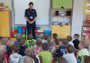 Pani policjantka stoi przy tablicy multimedialnej i opowiada o bezpieczeństwie podczas wakacji.