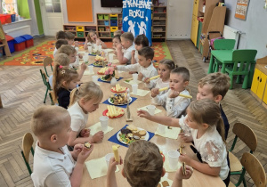 9. Dzieci z grupy „Motylki” w trakcie poczęstunku, siedzą przy wspólnym stole świętując uroczyste zakończenie roku przedszkolnego.