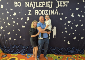 8. Zadowolony Franio u taty na rekach, obok stoi mama chłopca, wszyscy pięknie uśmiechają się do pamiątkowego zdjęcia.