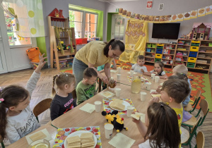 9. "Motylki" siedzą przy stoliku i degustują miód na waflach. Na stole widać także specjalnie przygotowaną lemoniadę z dodatkiem miodu.