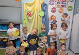 Dzieci pozują do wspólnego zdjęcia na tle dekoracji z okazji Dnia Kropki z wykonaną pracą plastyczną.