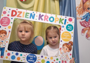 Dwie dziewczynki pozują do zdjęcia w fotoramce z okazji Dnia kropki.