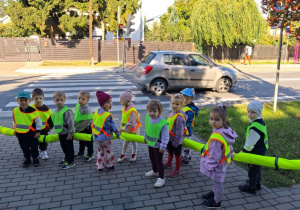 Dzieci stoją na chodniku i obserwują działanie sygnalizacji świetlnej.