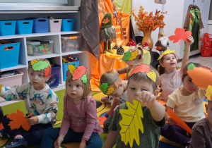 Dzieci siedzą na dywanie podczas zabawy rytmicznej z jesiennymi listeczkami.