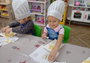 8. Dziewczynki w czapkach kucharskich kroją jabłka.