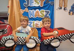10. Dwóch chłopców pozuje do zdjęcia z balonami w kształcie samochodów na tle dekoracji.