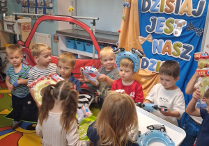 3. Chłopcy stoją w półkolu na tle dekoracji, dziewczynki trzymają tace z opaskami dla chłopców.