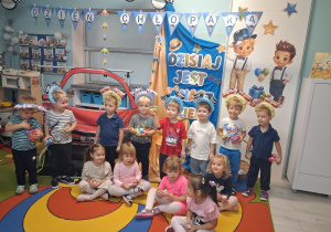 7. Zdjęcie grupowe dzieci na tle dekoracji z otrzymanymi upominkami.