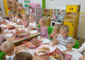 10. Dzieci siedzą przy stole i jedzą słodki poczęstunek.
