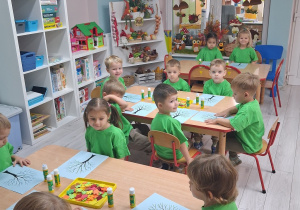 8.Dzieci siedzą przy stołach i naklejają na sylwetę drzewa jesienne liście.