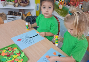 9.Dwie dziewczynki siedzią przy stole i wykonuje pracę plastyczną "Jesienne drzewo".