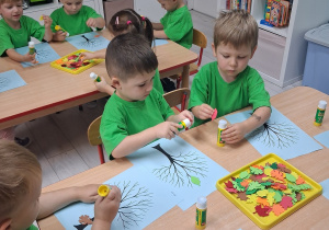 10.Grupka dzieci siedzi przy stole i wykonuje pracę plastyczną "Jesienne drzewo".
